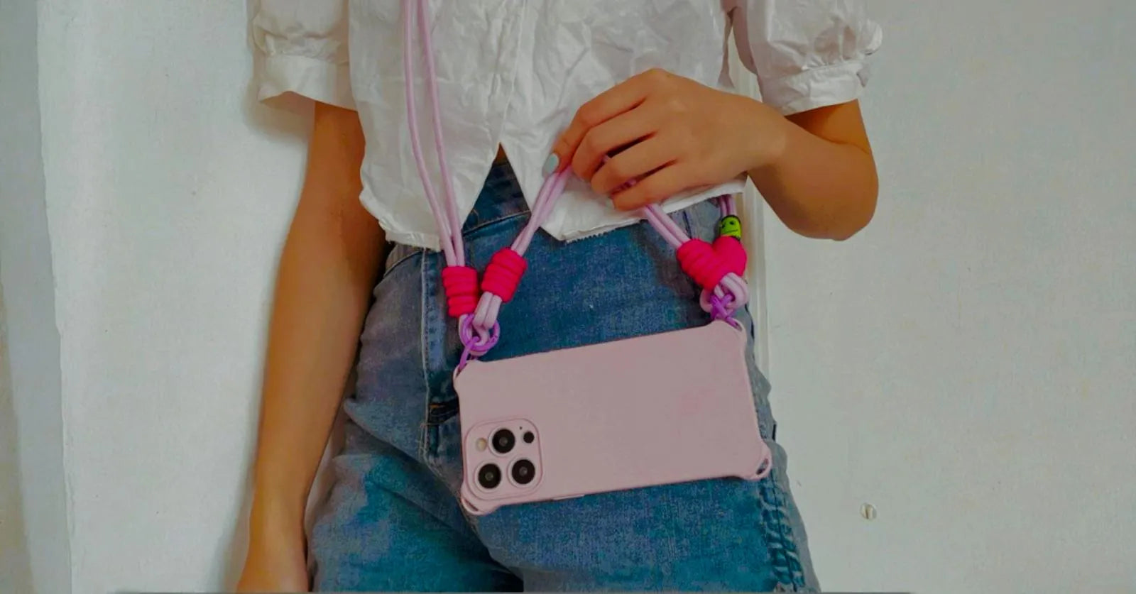 fond image produit coque iphone rose clair avec anse rose en utilisation sur mannequin avec jean et haut blanc
