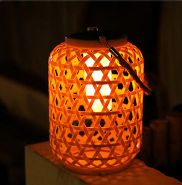 lampe exterieure tiki effet bambou posée sur un morceau de bois et allumée la nuit