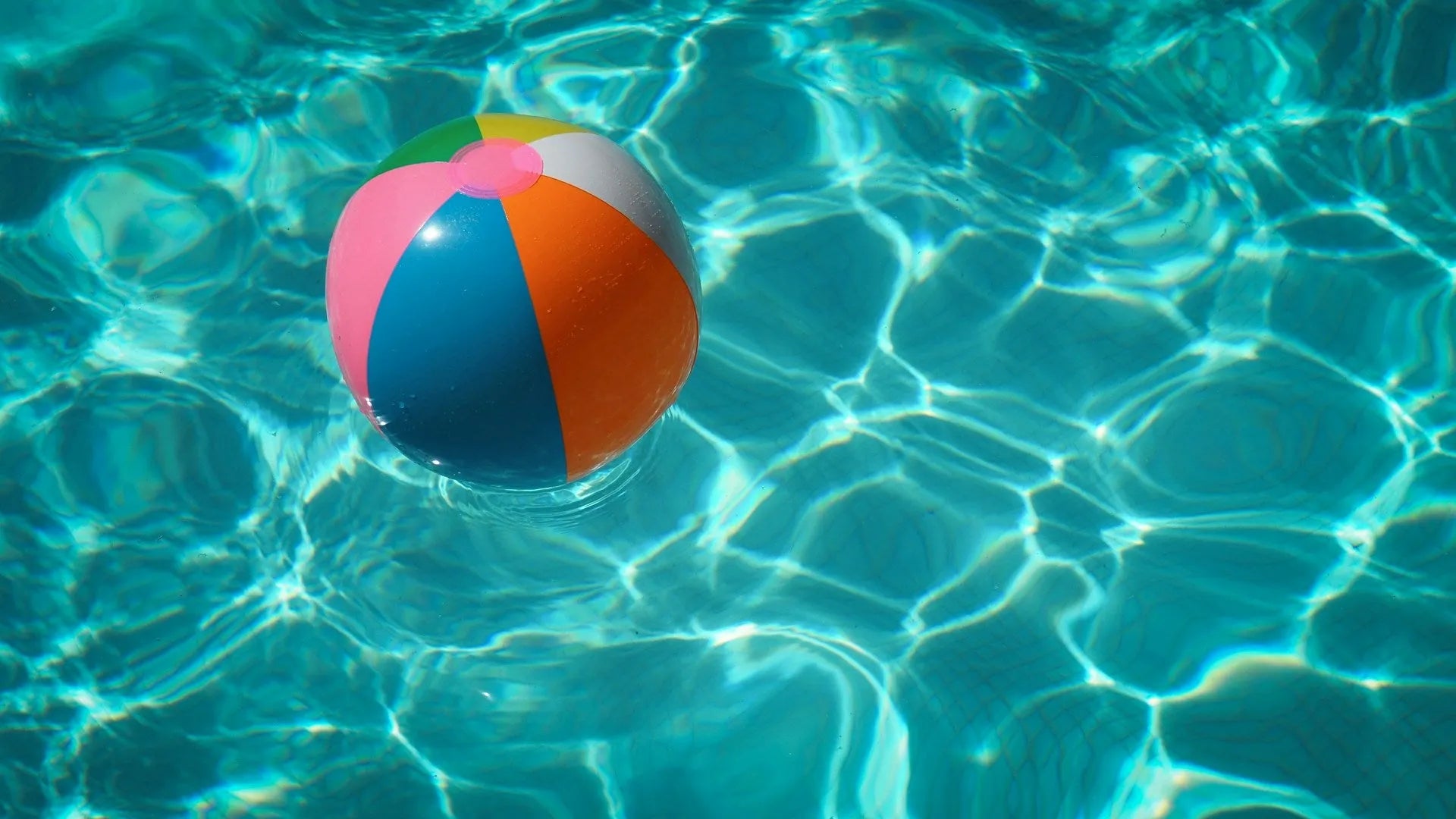 ballon gonflable multi couleur dans une piscine, avec reflets du soleil