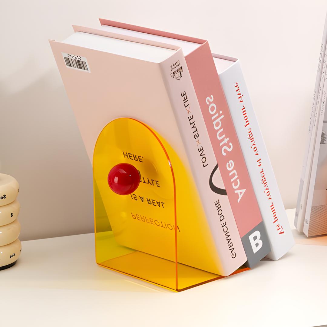 Bloc livres orange translucide avec boule rouge sur étagère blanche, supportant un livre grand format.