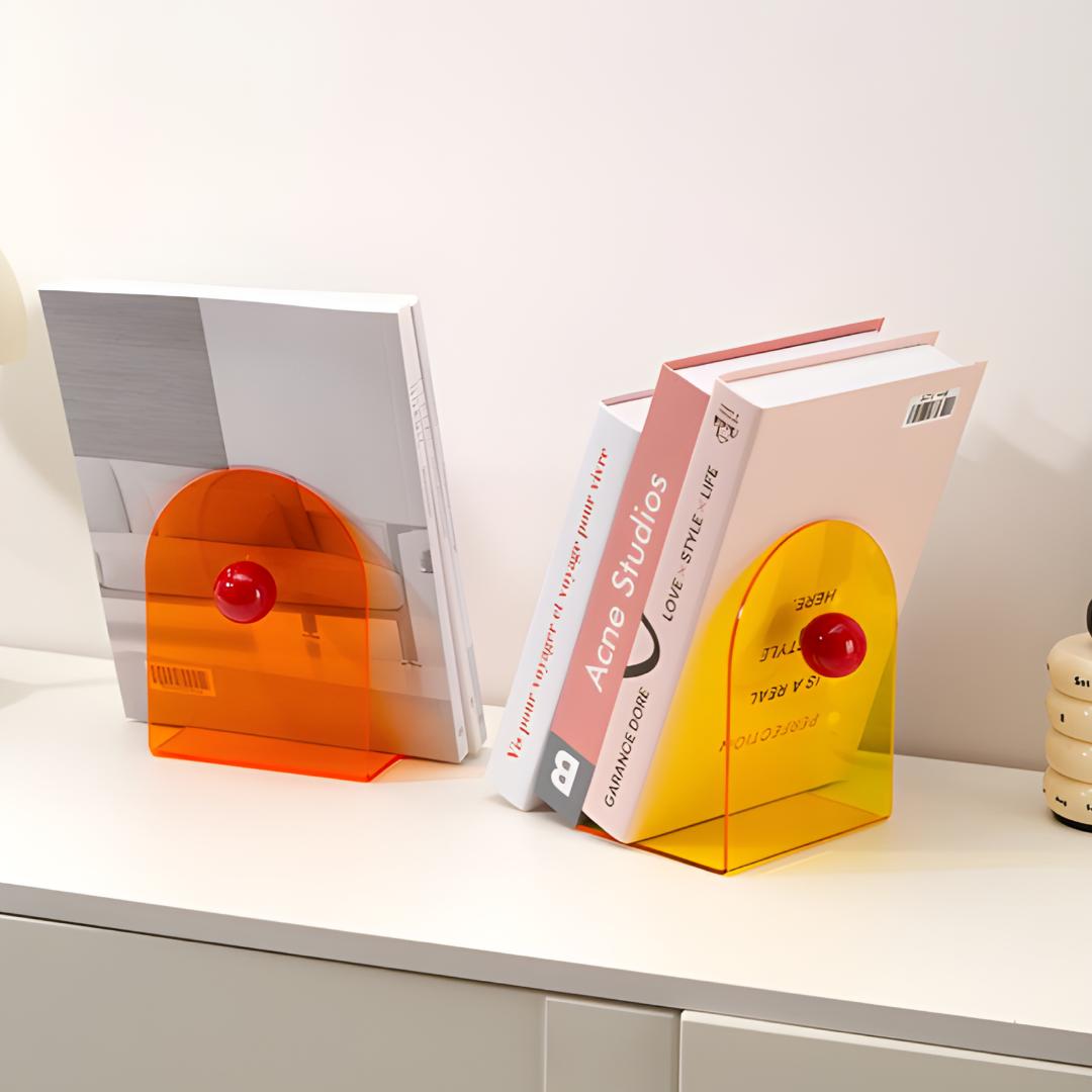 Bloc livres orange et bloc livres jaune en acrylique avec boule rouge, posés sur une étagère blanche