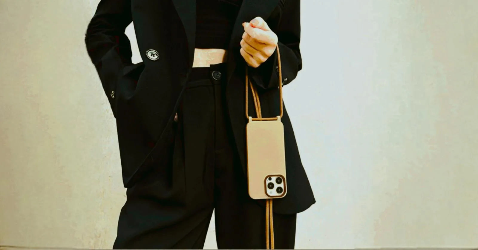 Vue large du look complet, coque crème pendue avec cordon marron sur tenue noire