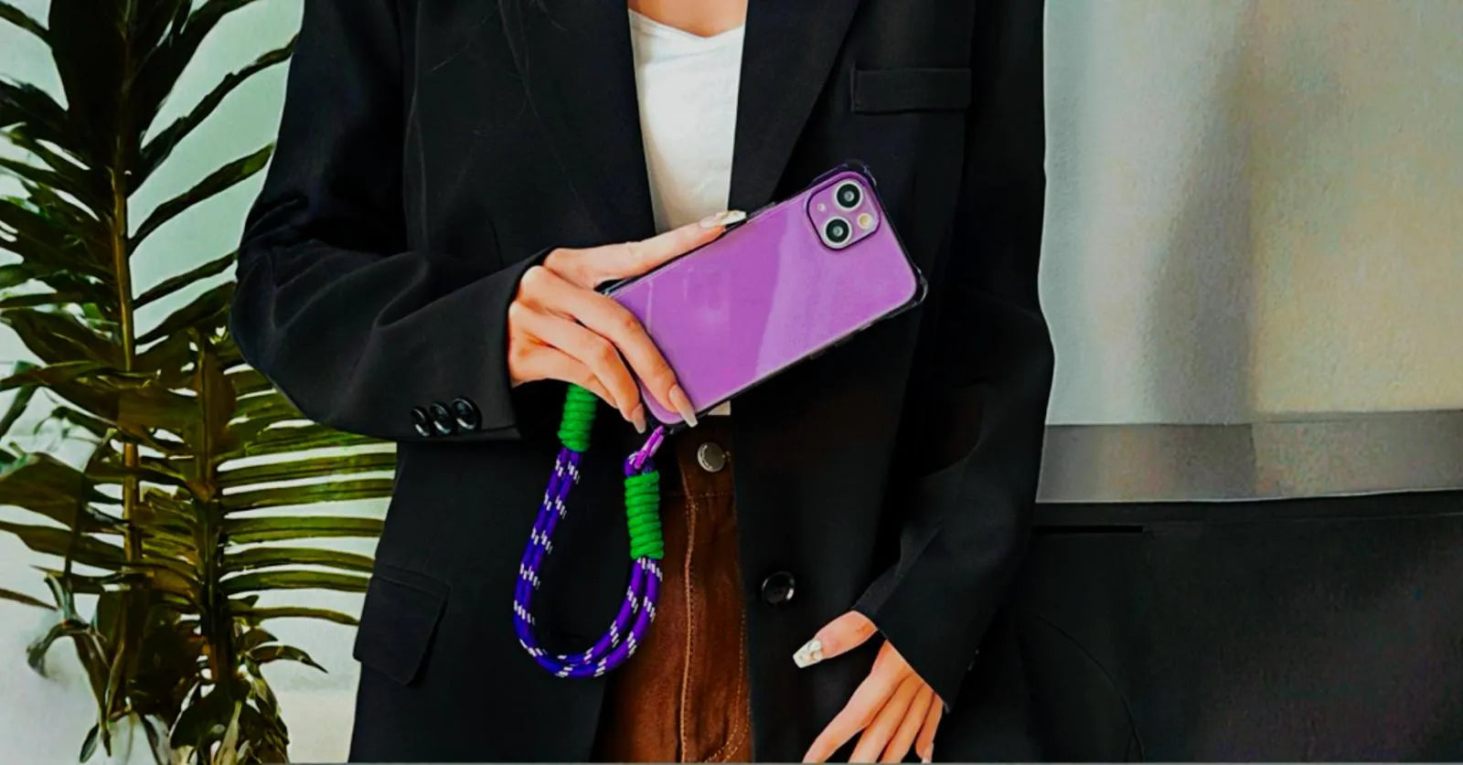 Coque iPhone violette tenue de profil par une femme en blazer noir devant une plante