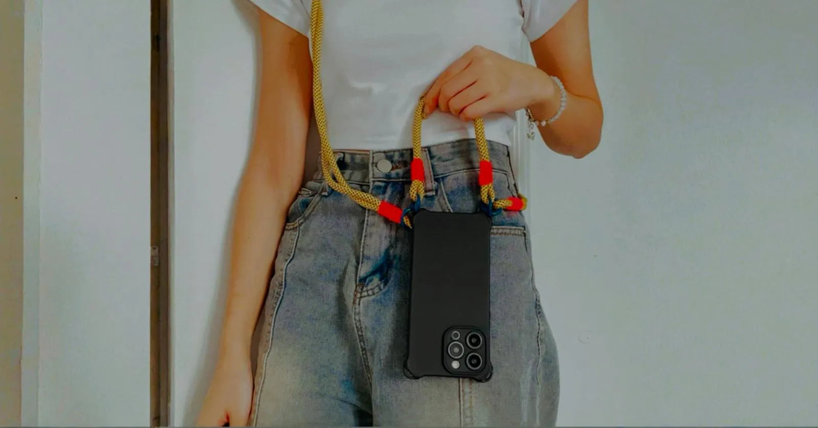 Coque noire portée en bandoulière, tenue à la main avec cordon jaune quadrillé et nœuds rouges fluo