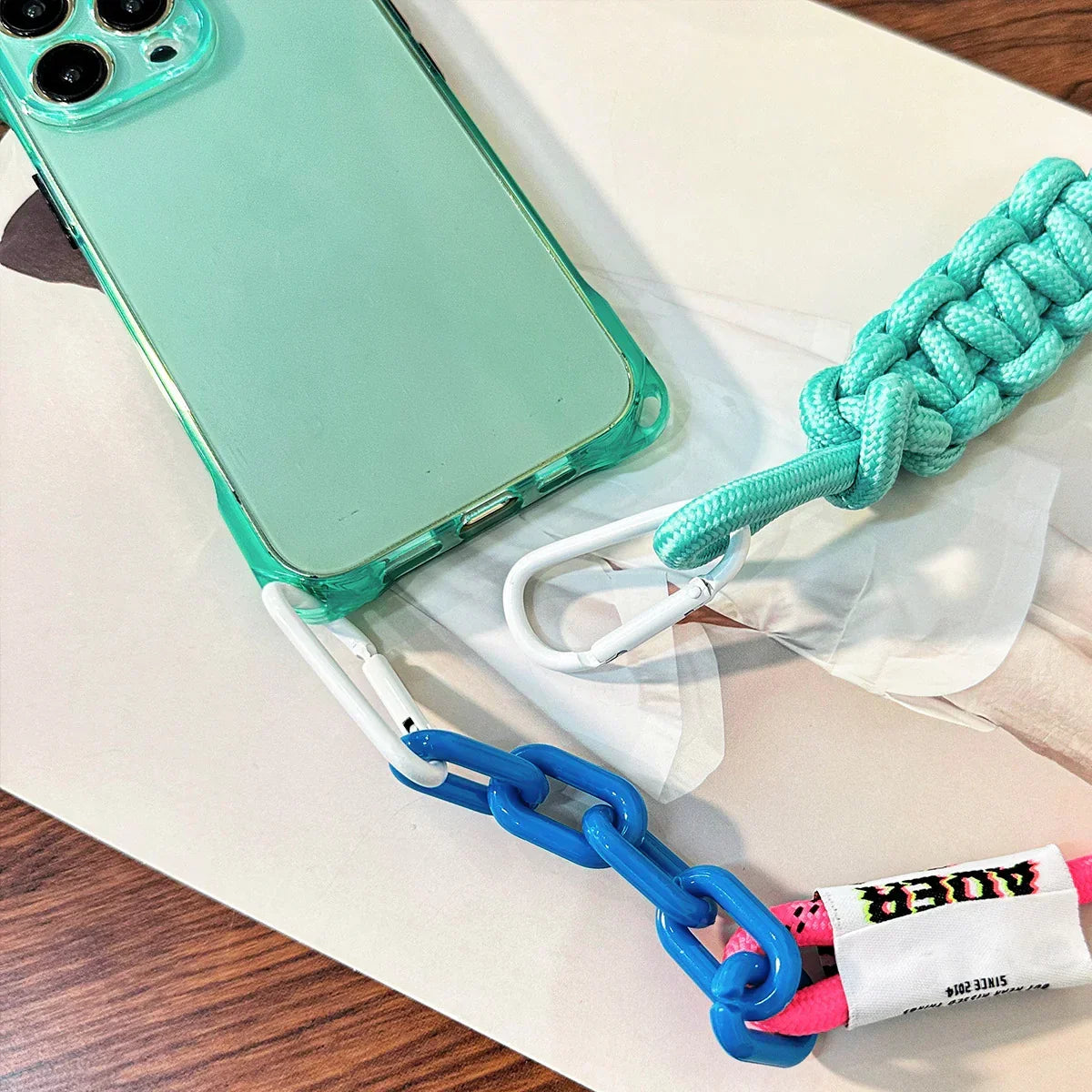 Détail du cordon fluo rose et bleu avec mousqueton et coque iPhone verte transparente