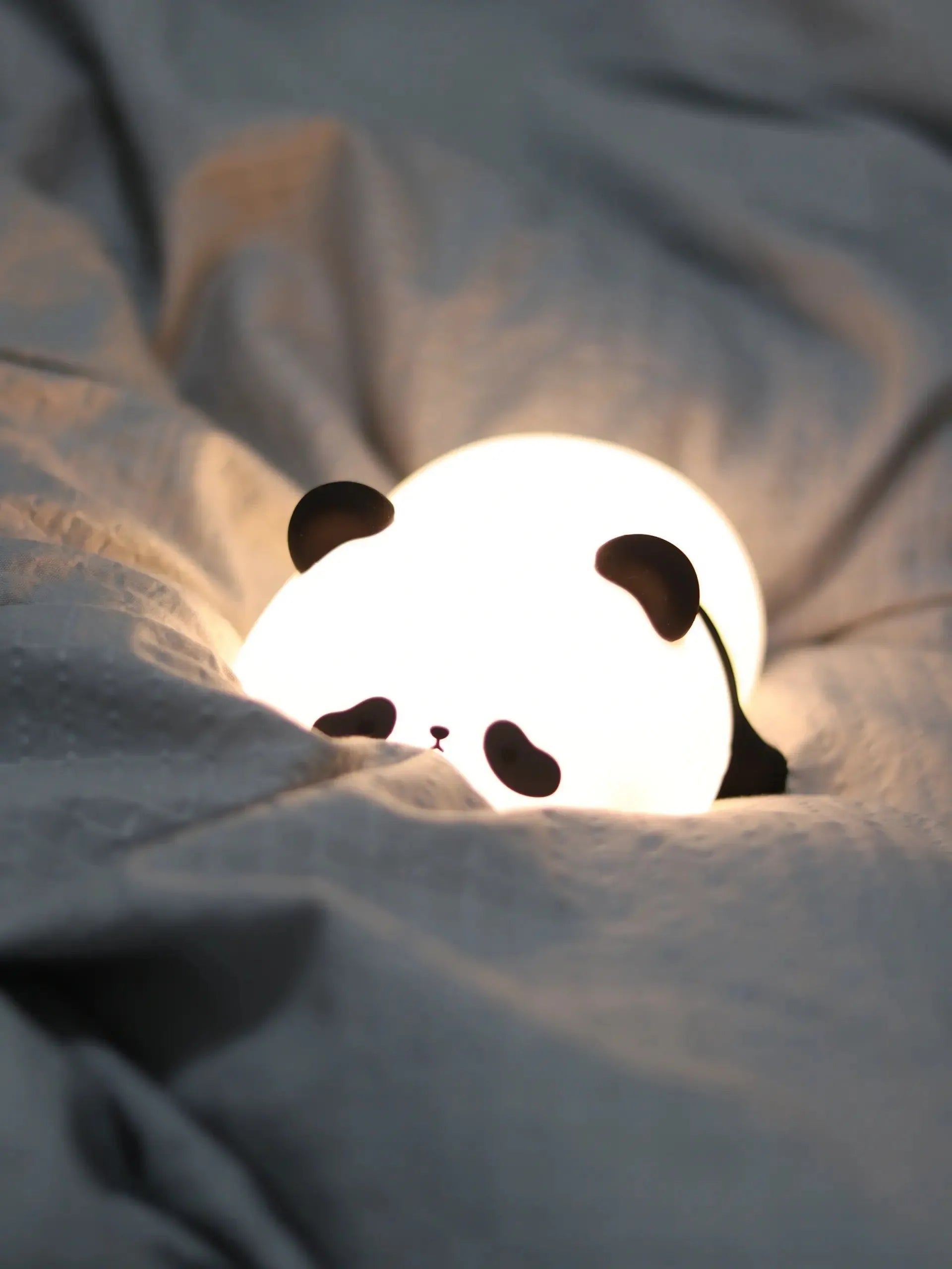 Veilleuse en forme de panda entre des draps, idéale pour rituels du coucher
