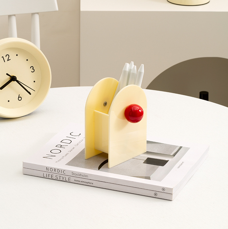 porte stylos style memphis bvlanc et rouge sur table blanche avec une horloge sur le coté