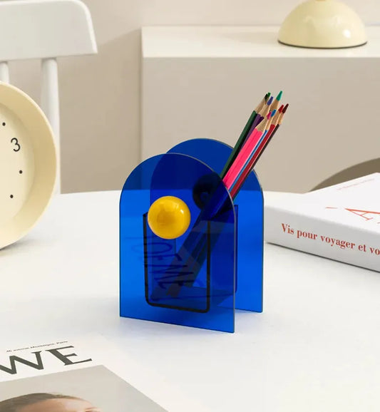 porte stylos style memphis bleu et jaune sur table blanche avec une horloge sur le coté