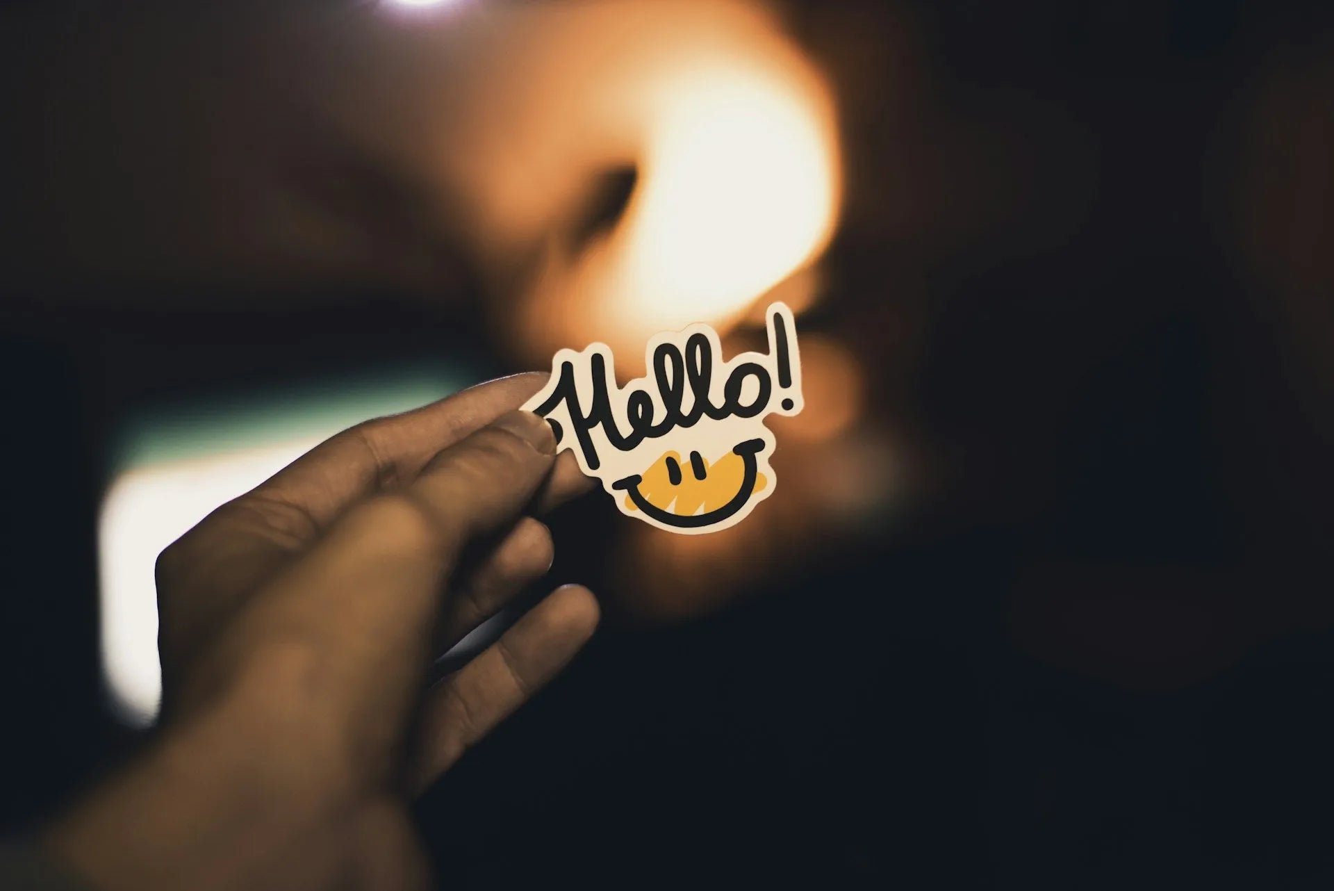 Main tenant un sticker “Hello”, design typographique sur fond sombre