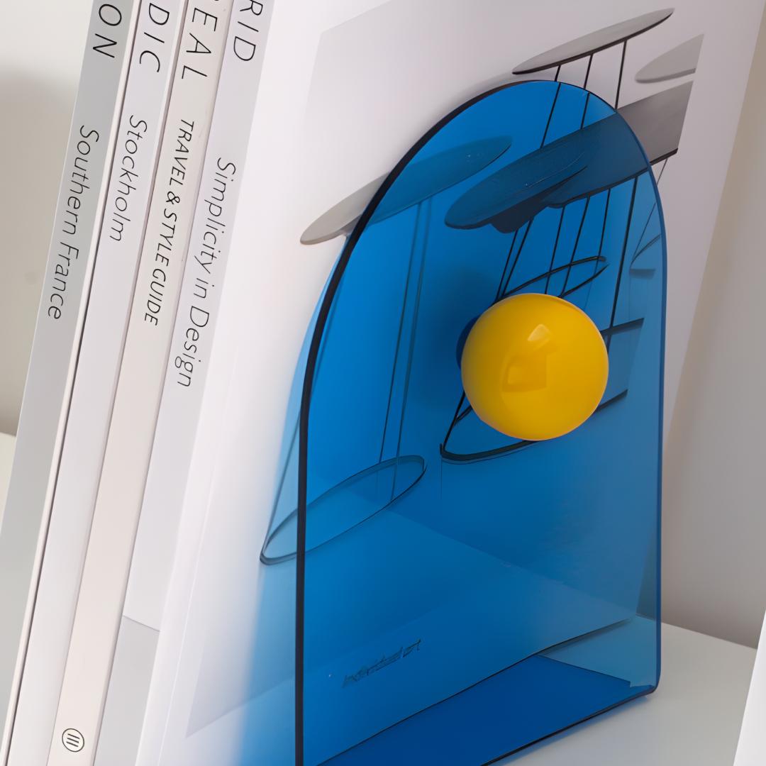 Zoom sur un bloc livres bleu translucide avec boule jaune, calant quatre livres blancs à couverture rigide.