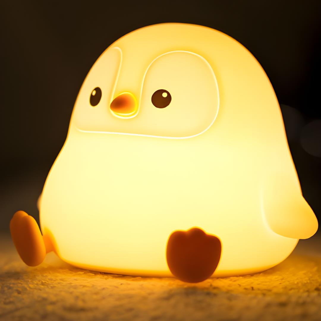 veilleuse originale en forme de pingouin assis allumée et posée sur un tapis