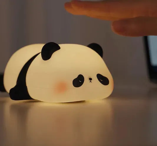 veilleuse panda allongée sur le ventre sur un bureau avec un main au dessus