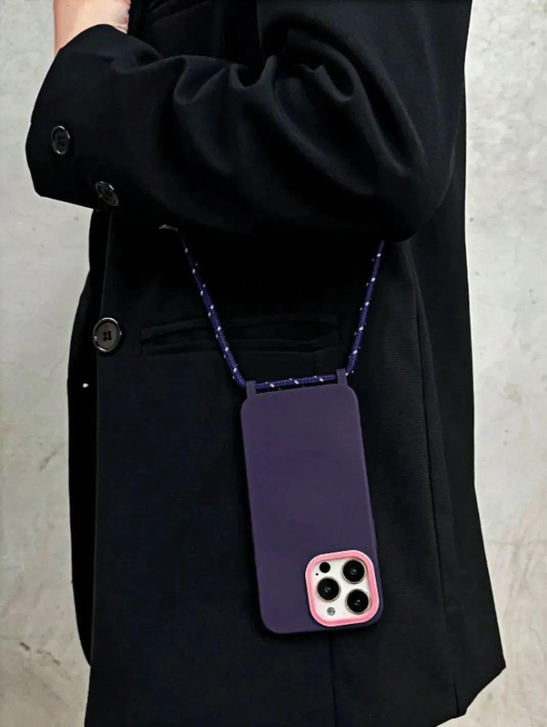 Coque violette portée à l’épaule sur une veste noire, fond mur béton