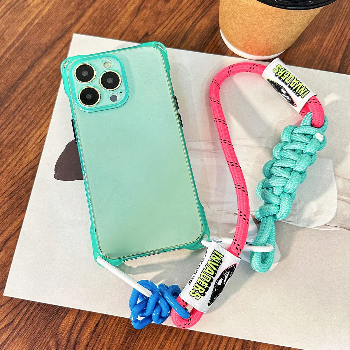 Coque fluo iPhone vert menthe avec cordon rose turquoise posée à plat – ambiance coffee table