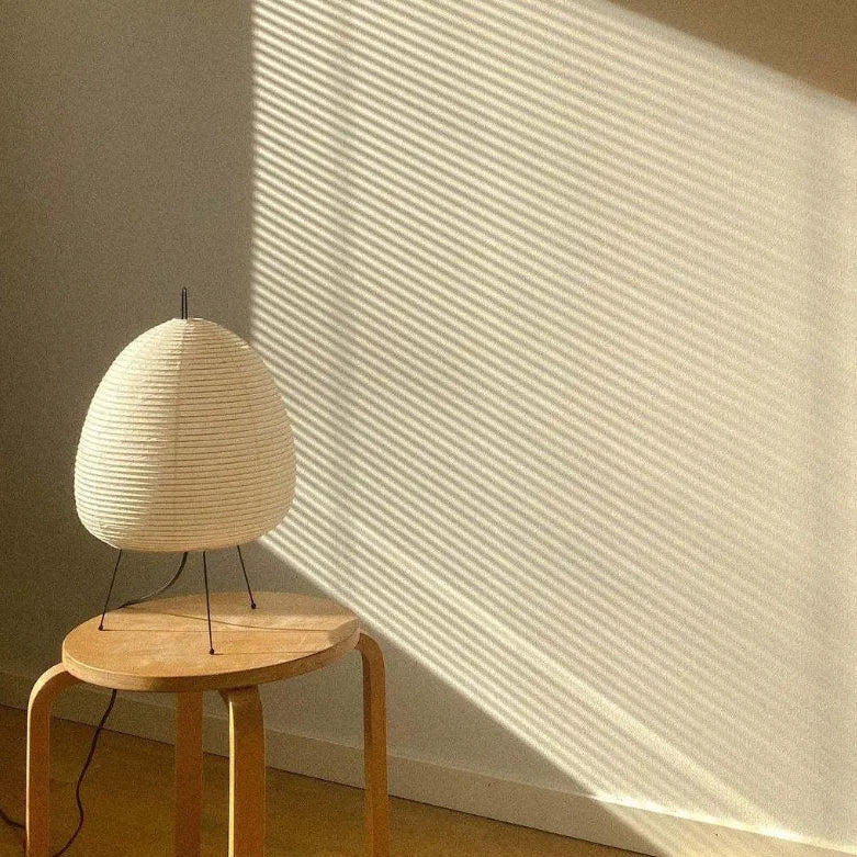 Lampe en papier Paper Moon blanche posée au sol, éclairée par un rayon de soleil à travers un store