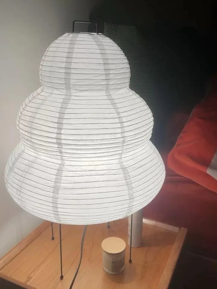 Lampe en papier posée sur une table de chevet en bois, idéale comme lumière d’appoint de nuit
