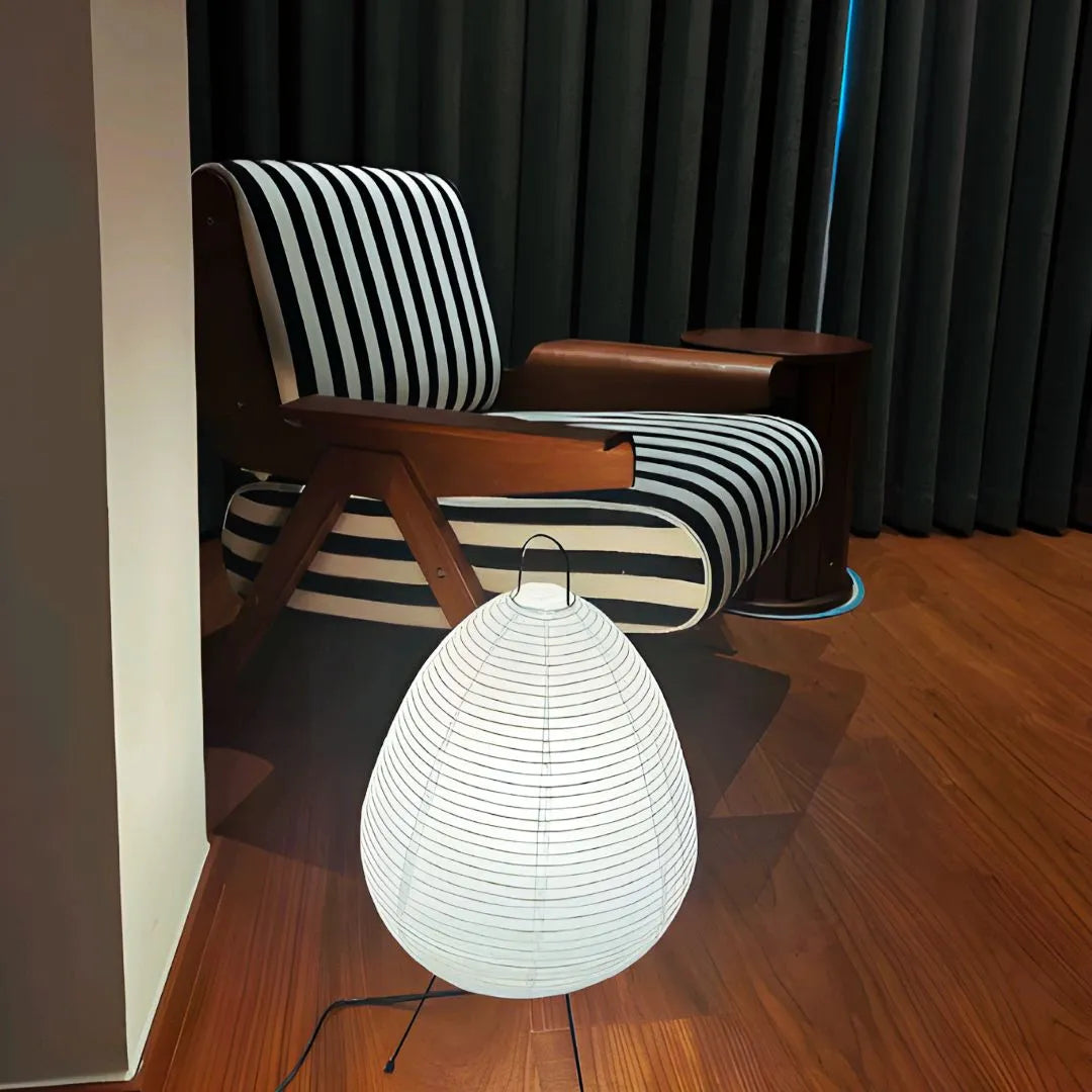 Lampe d’appoint en papier blanc posée au sol dans un salon moderne avec fauteuil graphique rayé noir et blanc