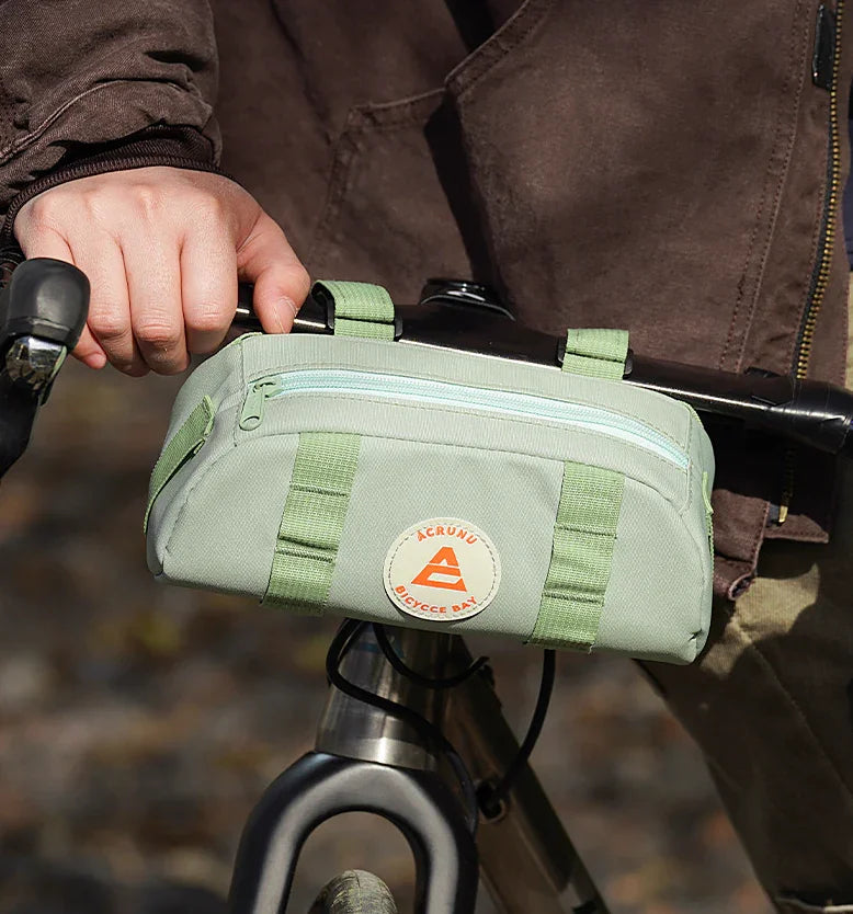 Cycliste tenant un sac de guidon vert sur fond automnal – accessoire vélo compact et léger