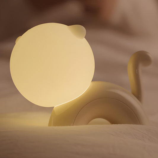 veilleuse chat en silicone et abs allumée et posée sur un lit et des draps blancs