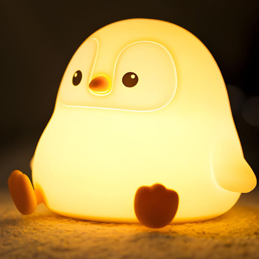 veilleuse originale en forme de pingouin assis allumée et posée sur un tapis
